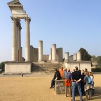 Touristengruppe betrachtet rekonstruierten römischen Tempel mit hohen Säulen im Archäologischen Park Xanten unter blauem Himmel.