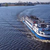 Weiß-blaues Passagierschiff MS Clair d'Étoile fährt auf ruhigem blauen Wasser mit Kielwasser dahinter. Industrieküste im Hintergrund sichtbar.