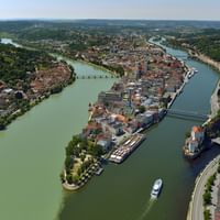 Luftaufnahme des Passauer Drei-Flüsse-Ecks, wo Donau, Inn und Ilz zusammenfließen, mit der historischen Altstadt und bunten Gebäuden.