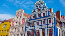 Row of ornate historic buildings in Stettin with blue, pink, and yellow facades. The blue building features decorative white stucco and red windows.