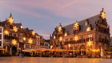 Historic buildings in Nijmegen decorated with illuminated star ornaments at twilight. Market stalls line the cobblestone square during Advent season.