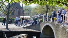 Steinbogenbrücke mit weißen Geländern über einem Kanal in Enkhuizen. Besucher gehen über die Brücke zum Zuiderzeemuseum.