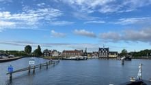 Harbor view of Huizen with traditional Dutch houses along the waterfront, wooden pier extending into calm water under blue sky with clouds.
