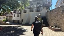 Wanderer mit Rucksack auf historischem Platz in Bodenheim mit traditionellen Fachwerkhäusern und Steinmauern bei sonnigem Wetter.