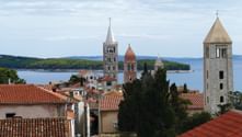 Mittelalterliche Stadt Rab mit steinernen Glockentürmen und roten Ziegeldächern mit Blick auf die blauen Gewässer der Kvarner Bucht.