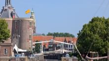 Weiße Zugbrücke über Kanal in Enkhuizen mit historischem Backsteinturm mit grüner Kuppel, oranger Flagge und traditionellen niederländischen Gebäuden.