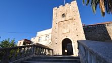 Steinernes Stadttor mit Bogendurchgang in Korčula, erreichbar über Steintreppen mit Balustraden. Klarer blauer Himmel und Palme sichtbar.