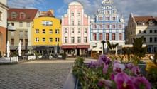 Row of colorful historic buildings in Stettin with ornate facades. Pink and blue decorated buildings stand beside yellow and beige houses. Purple flowers in foreground.