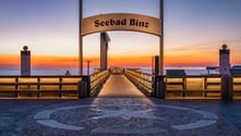Entrance to Seebad Binz pier on Rügen with decorative compass rose pavement at sunset. The illuminated pier extends into the Baltic Sea.