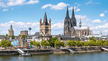 Cologne skyline with the Gothic Cologne Cathedral and Romanesque Great St. Martin Church along the Rhine River under blue sky with white clouds.