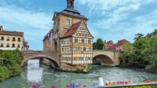 Bamberg's famous Old Town Hall with half-timbered facade built on a bridge over the Regnitz river, surrounded by colorful historic buildings.