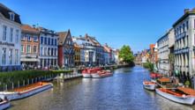Historic canal with boats in Ghent Canal in Ghent lined with colorful historic buildings and tour boats. Medieval architecture with stepped gables reflects in the water under blue sky.