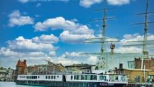 River cruise ship MS Princess with white and turquoise hull moored in Stralsund harbor, with historic buildings and tall ship masts in background.