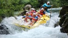 Gelbes Raft mit sieben Personen in Helmen und Schwimmwesten in Wildwasser-Stromschnellen bei Omiš, umgeben von Felsen und grüner Vegetation.