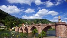 Historische Sandsteinbrücke mit mehreren Bögen über den Neckar in Heidelberg, mit einer Statue auf dem Brückenturm.