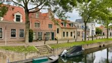 Kanal in Medemblik mit vertäuten Booten entlang einer baumgesäumten Kaimauer. Traditionelle holländische Backsteinhäuser mit roten Ziegeldächern säumen das Ufer.