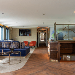 Eleganter Salon auf der Magnifique X mit blauem Samtsofa, gemusterten Kissen, Holzrezeption und Fischgrätparkett.