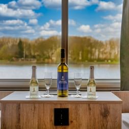 Oberdeckkabine der MS Princess mit Weinflaschen und Gläsern auf Holztisch, großes Fenster mit Blick auf Fluss und Bäume.