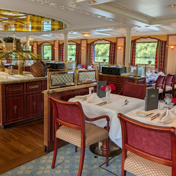 Elegantes Restaurant an Bord der Casanova mit burgunderroten Polsterstühlen, weiß gedeckten Tischen, Holzbuffet und großen Fenstern mit Blick aufs Wasser.