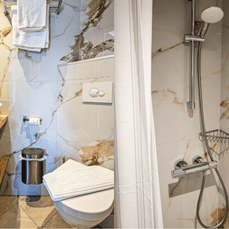 Kompaktes Badezimmer mit Marmorfliesen, Holzwaschtisch mit weißem Becken, Wandtoilette und verglaster Dusche mit Chromarmaturen.