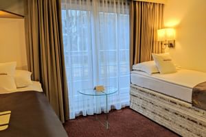 2-Bett-Kabine auf MS Classica mit zwei Einzelbetten, weißer Bettwäsche, beigen Vorhängen, Wandlampe, Glastisch und bordeauxrotem Teppich.