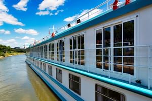 White river cruise ship MS Switzerland with turquoise trim and large windows moored on a calm river under blue sky with white clouds.