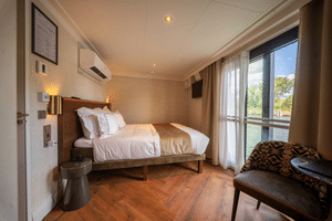 Modern suite on Magnifique X with double bed, wooden flooring, air conditioning, and large windows overlooking a river with green landscape.