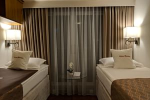 2-Bett-Kabine auf MS Classica mit zwei Betten, beigen Vorhängen, Wandlampen und Zierkissen. Kleiner Tisch mit Orchidee zwischen den Betten.