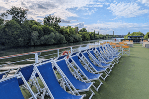 Sonnendeck der Casanova mit Reihen blau-weißer Liegestühle entlang der Reling. Fluss mit grünen Bäumen und anderem Schiff im Hintergrund.