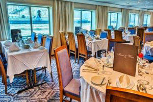 Elegant restaurant on SE Manon with tables set with white linens, wine glasses, and menu cards. Large windows overlook the waterfront.
