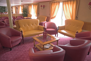 Geräumiger Salon auf dem Schiff Provence mit gelben Sofas, rosa Sesseln, Holzcouchtisch, pfirsichfarbenen Vorhängen und rosa Teppich.