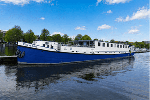 Flusskreuzfahrtschiff Clair de Soleil mit blauem Rumpf und weißem Aufbau am Kai. Bäume und Gebäude im Hintergrund unter blauem Himmel.