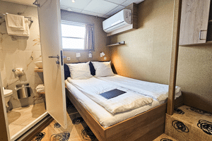Compact upper deck cabin on MS Nassau with double bed, white linens, ensuite bathroom, window, air conditioning, and patterned carpet.