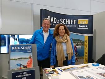 Zwei SE-Tours Mitarbeiter an ihrem Messestand mit Rad & Schiff Broschüren und Werbematerialien auf dem Tisch.