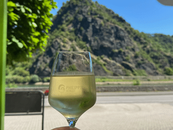 Glas Weißwein mit dem berühmten Loreley-Felsen im Hintergrund am Rhein unter blauem Himmel.