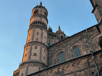 Aufwärtsblick auf den Wormser Dom mit rundem Steinturm und romanischer Architektur mit Bogenfenstern vor blauem Himmel in der Dämmerung.
