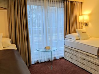 Twin cabin on MS Classica with two single beds, white bedding, beige curtains, wall lamp, glass table, and burgundy carpet.