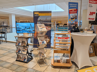 Messestand mit Kempf-Branding, Prospektständern und Werbematerialien in einem Einkaufszentrum. Ein Monitor und Banner werben für Flusskreuzfahrten.