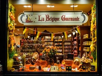 Schaufenster der Schokoladerie La Belgique Gourmande mit belgischen Flaggen, Schokoladenregalen und herbstlicher Dekoration im Fenster.