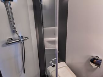 Kompaktes Badezimmer auf der MS Princess mit Glasduschtür, weißer Toilette, Chromarmaturen und grauem Boden in einer modernen Schiffskabine.