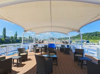 Sun deck of MS SE-MANON featuring dark wicker furniture arranged under a white canopy. Wooden decking with multiple seating areas and river view.