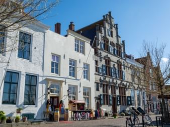 Reihe historischer niederländischer Gebäude in Veere mit verzierten Treppengiebeln, weißen Fassaden und großen Fenstern. Fahrräder und Geschäfte auf Kopfsteinpflaster.