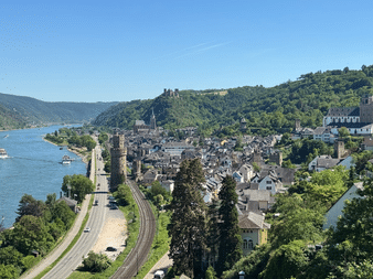 Luftaufnahme von Oberwesel, einer historischen Stadt am Rhein mit mittelalterlichen Türmen, Kirchtürmen und Weinbergen unter blauem Himmel.