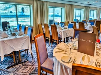 Elegant restaurant on SE Manon with tables set with white linens, wine glasses, and menu cards. Large windows overlook the waterfront.