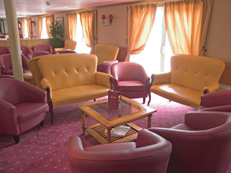 Geräumiger Salon auf dem Schiff Provence mit gelben Sofas, rosa Sesseln, Holzcouchtisch, pfirsichfarbenen Vorhängen und rosa Teppich.