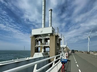 Große Betonstruktur der Deltawerke-Sturmflutsperre in Zeeland mit hohen Schornsteinen, von einer Straße mit weißen Geländern betrachtet.