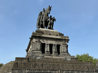 Großes Steinmonument in Koblenz mit Reiterstatue auf der Spitze. Die Struktur hat einen gestuften Sockel mit Reliefs und Bogenöffnungen.