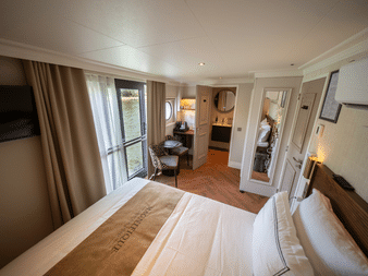 Elegante Flusskreuzfahrt-Suite mit Doppelbett, Balkontür, Sitzbereich, Kleiderschrank und warmem Holzboden auf dem Oberdeck der Magnifique X.