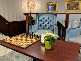 Elegant salon on MS Classica with blue velvet armchairs, chess set on wooden table, decorative lamp, and framed artwork on striped walls.