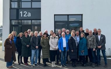 Gruppe von etwa 25 Reiseleitern, die vor einem modernen Gebäudeeingang mit der Aufschrift '12a' stehen, gekleidet in Winterkleidung.